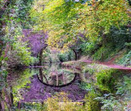 A canal bridge is reflected in flat, calm water. a canal bridge is reflected in the flat calm water of the canal