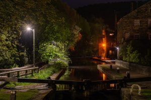 Night on the Canal Night scene of a canal with brick buildings, trees, and lit street lamps reflecting in the water, at night.