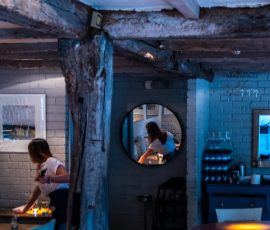 Dimly lit restaurant interior with blue chairs, brick walls, and candles on a table. Dimly lit restaurant interior with blue chairs, brick walls, and candles on a table.